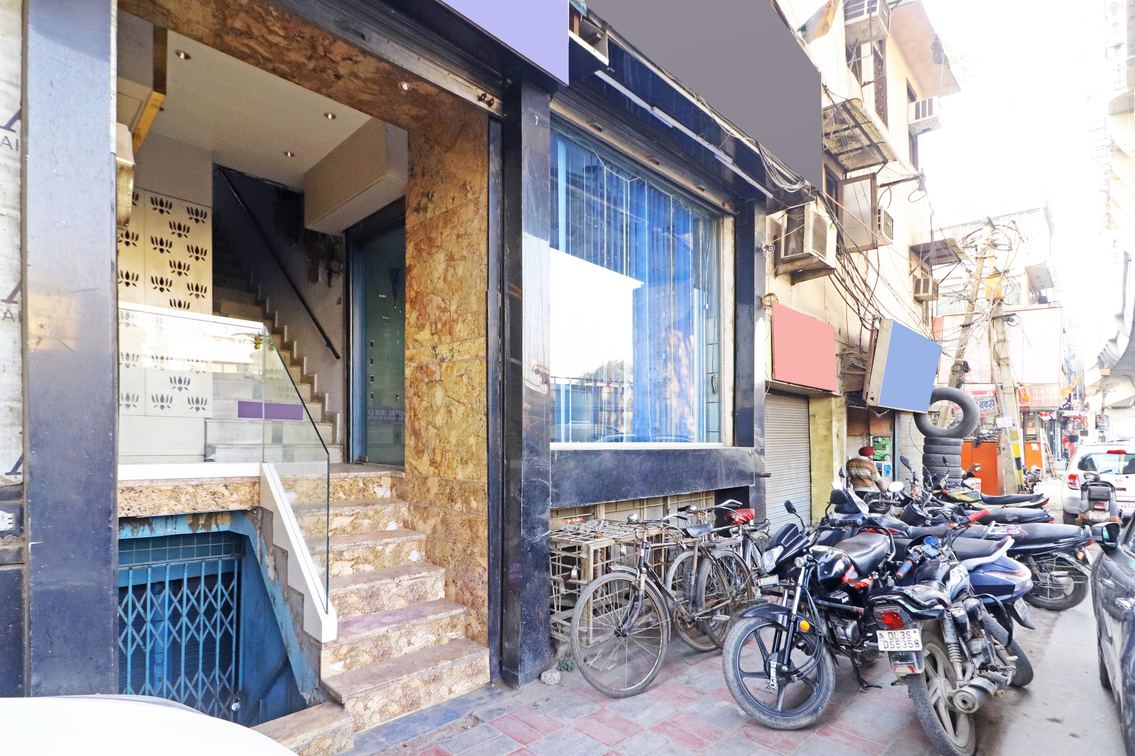 A building with a staircase leading to an entrance, a window with a blue frame, and several motorcycles parked outside.