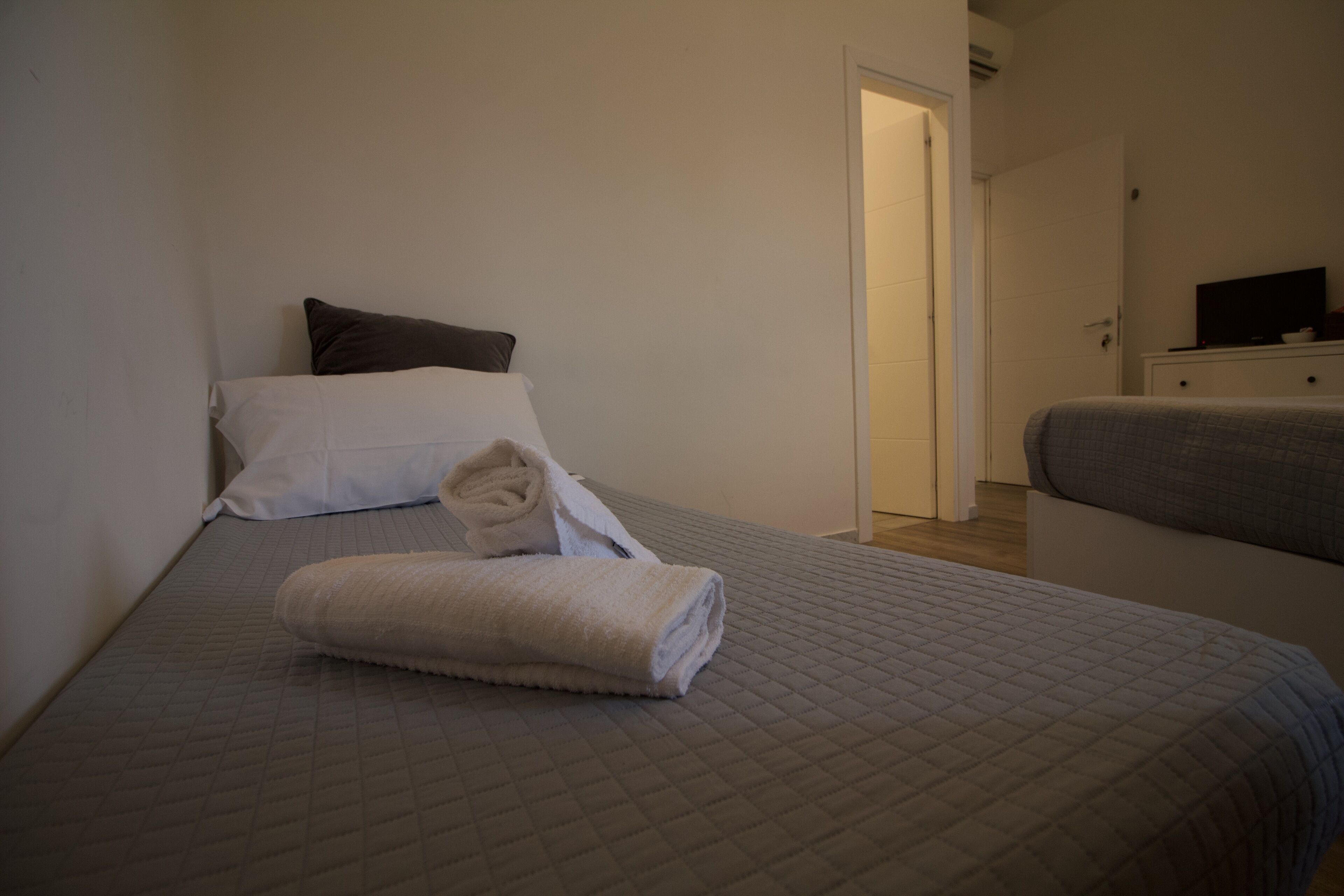 A neatly made bed with a quilted bedspread, a folded towel, and a pillow.