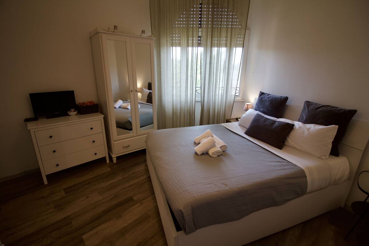 Makuuhuone, jossa on sänky, vaatekaappi, televisio ja ikkuna, jossa on verhot.
