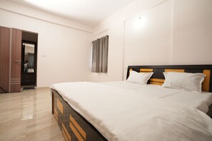 A bedroom with a bed, wooden headboard, white bedding, a door, and a curtain. - Srushti Service Apartment (Bengaluru)