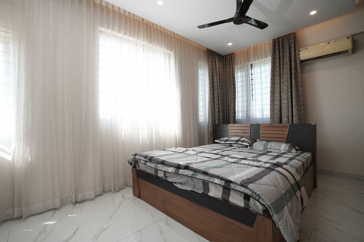 A bedroom with a bed, curtains, a ceiling fan, and an air conditioning unit.