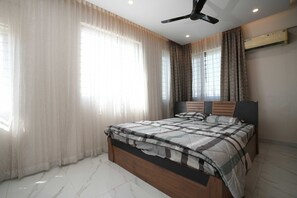 A bedroom with a bed, curtains, a ceiling fan, and an air conditioning unit. - Srushti Service Apartment (Bengaluru)
