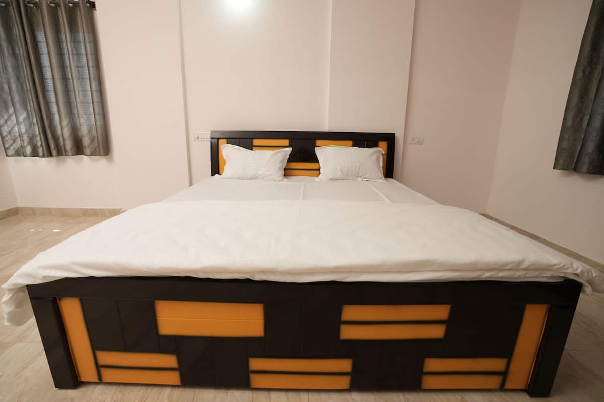 A bed with a black and orange headboard, white bedding, and a plain wall with a light switch.