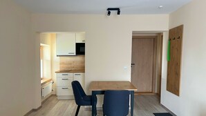 A small, modern kitchen with white cabinets and a wooden countertop. There is a dining table with two chairs in the center of the room.