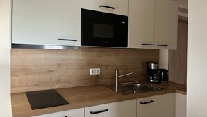 A modern kitchen with white cabinets, a black microwave, a stainless steel sink, and a coffee maker.