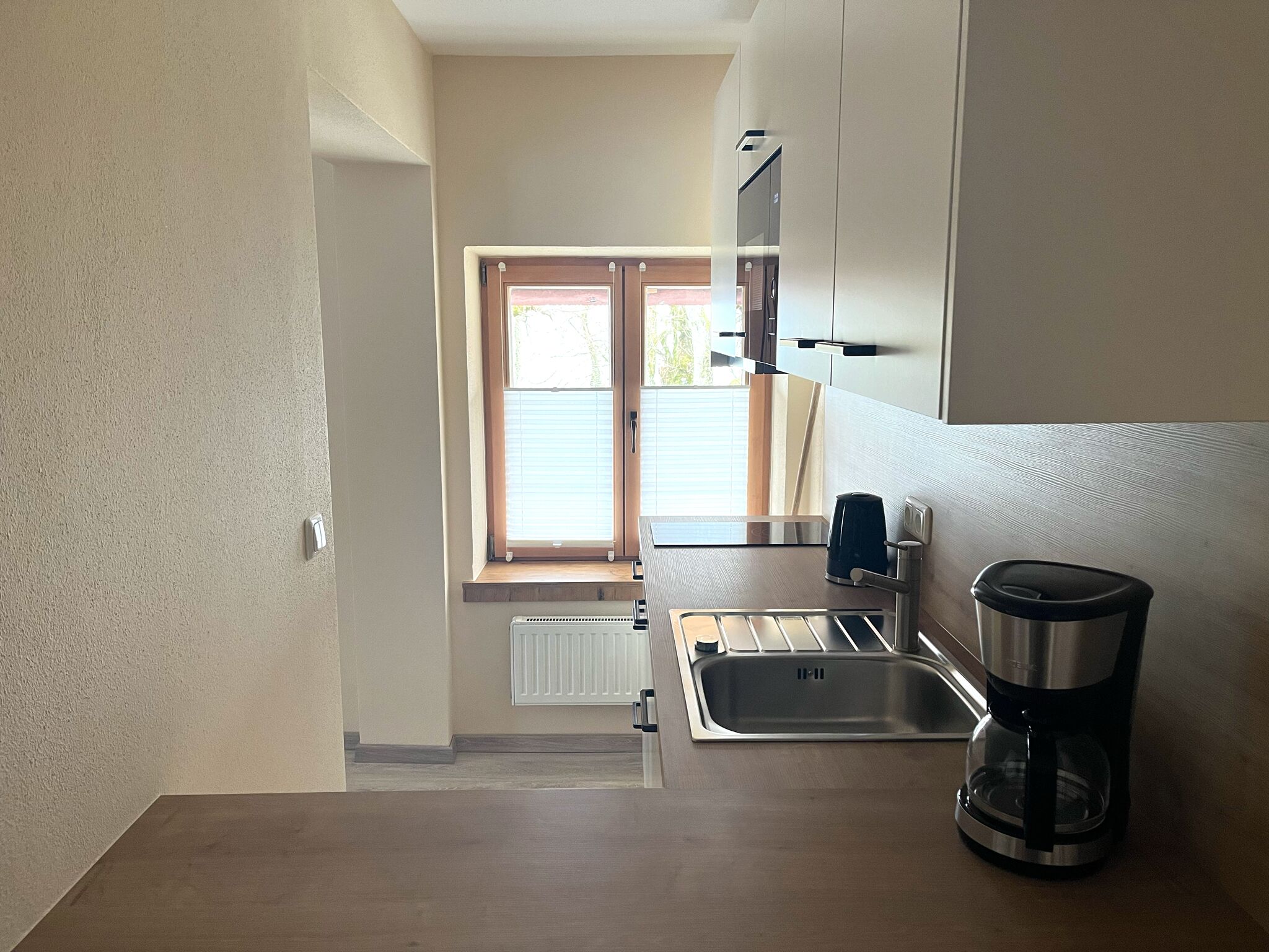 A compact kitchen with a window, a sink, a coffee maker, and a built-in oven.