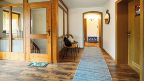 A wooden interior with a hallway leading to a door, a chair, and a rug.
