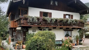 A two-story chalet with a balcony adorned with flowers, a stone pathway, and a well-maintained garden.