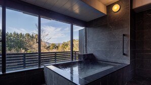 A modern spa area with a large window, a hot tub, and dark marble walls. - Sengokubara cocon (Hakone)