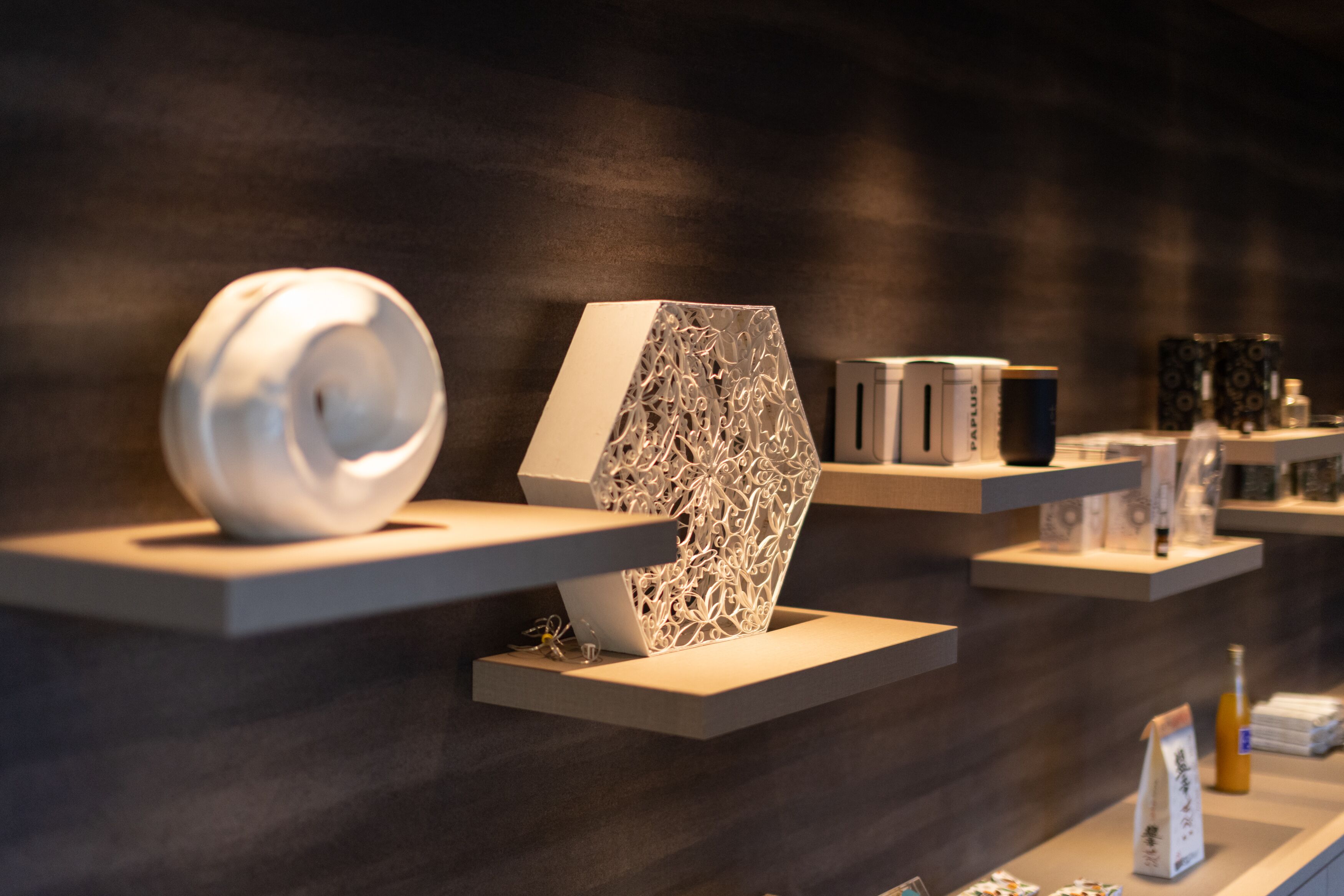 A modern interior with geometric sculptures on shelves, a dark wall, and a few items on a counter.