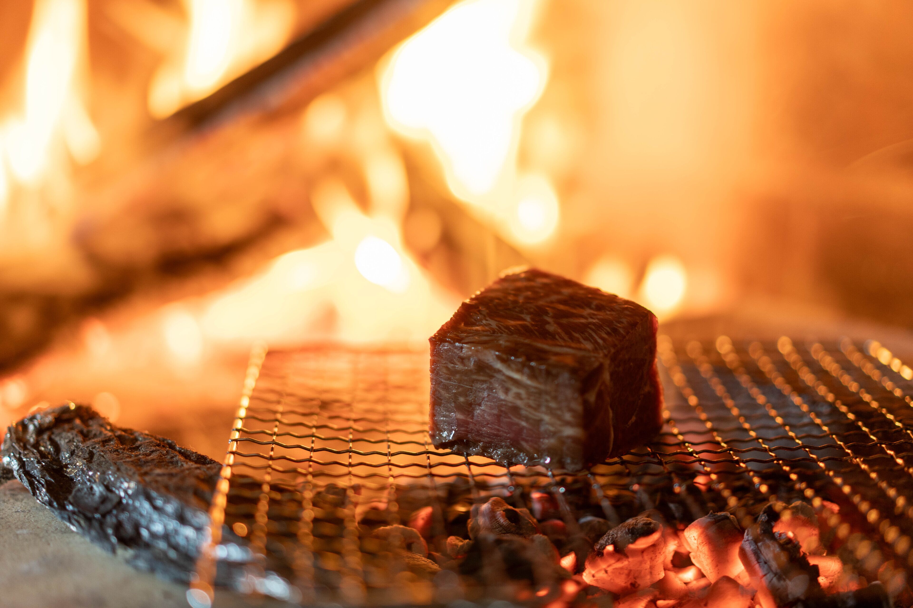 A steak grilling over an open flame with a wire rack.