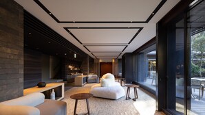 A modern interior with a sofa, ottoman, and small tables, a fireplace, and a view through large windows. - Sengokubara cocon (Hakone)