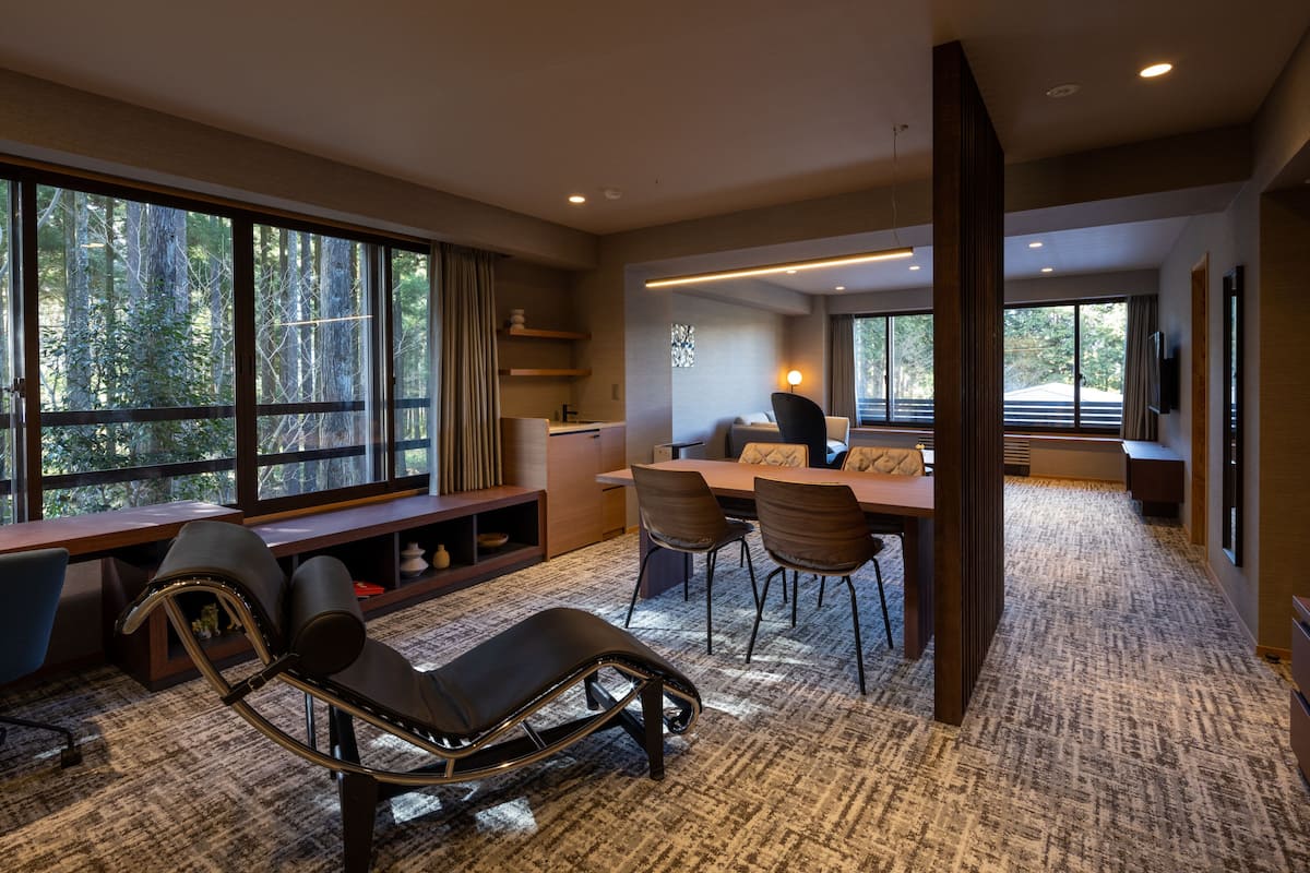 Una habitación de hotel moderna con un ventanal grande, un escritorio, un sillón y un comedor.