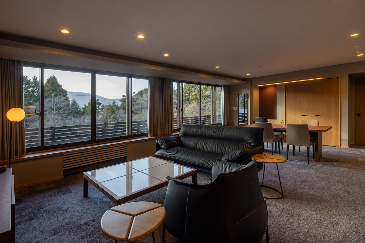 Una sala de estar moderna con un sofá de cuero, una mesa de centro de vidrio y un comedor con una mesa y sillas de madera.