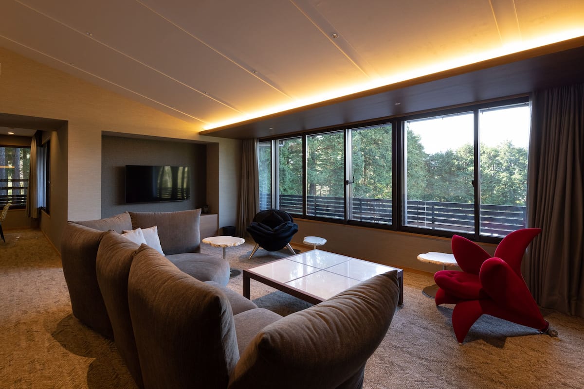 Una sala de estar moderna con un ventanal grande, un televisor de pantalla plana, un sofá, una mesa de centro y una silla roja.