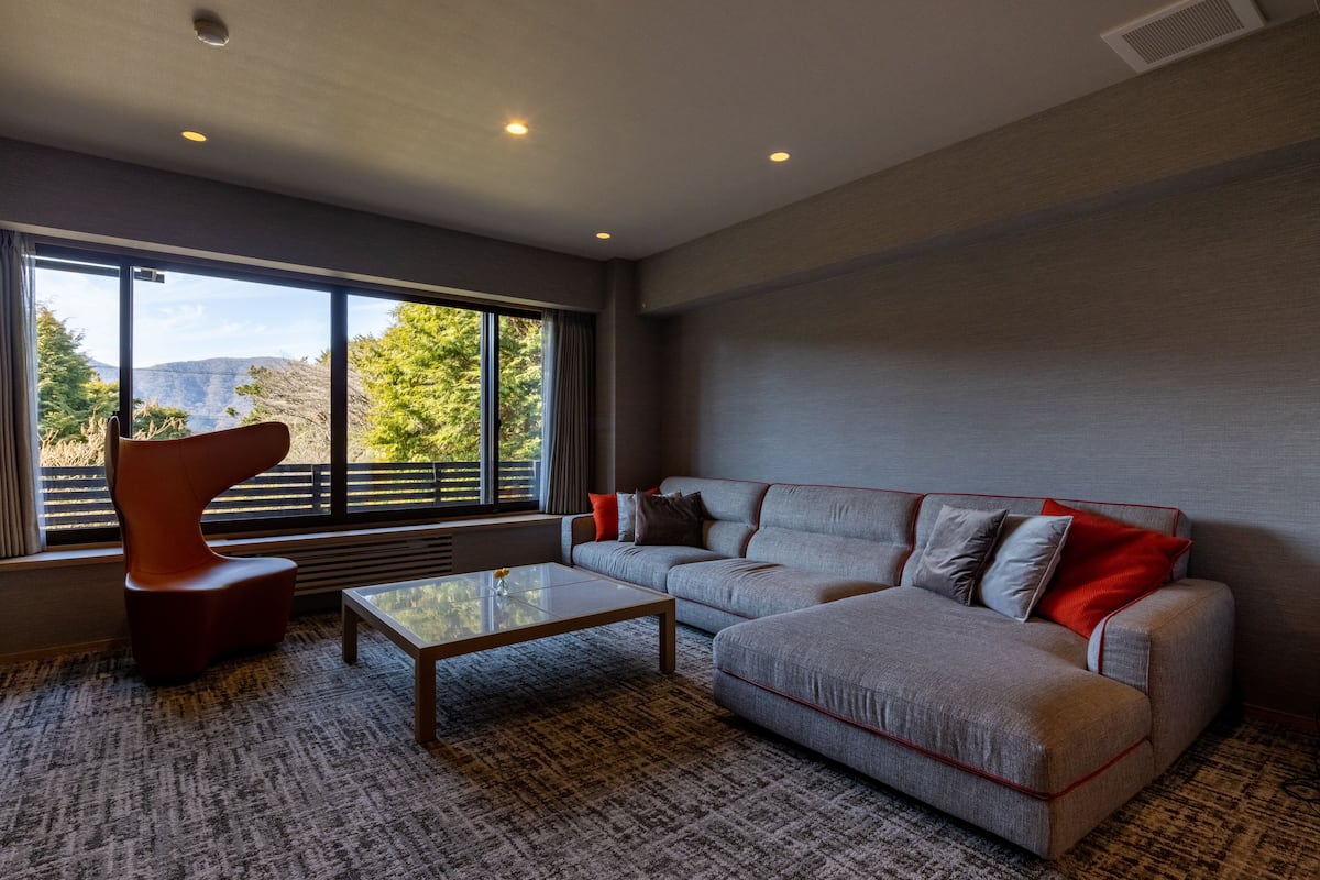 Una sala moderna con un sofá modular, una mesa de centro de vidrio y una silla naranja singular.