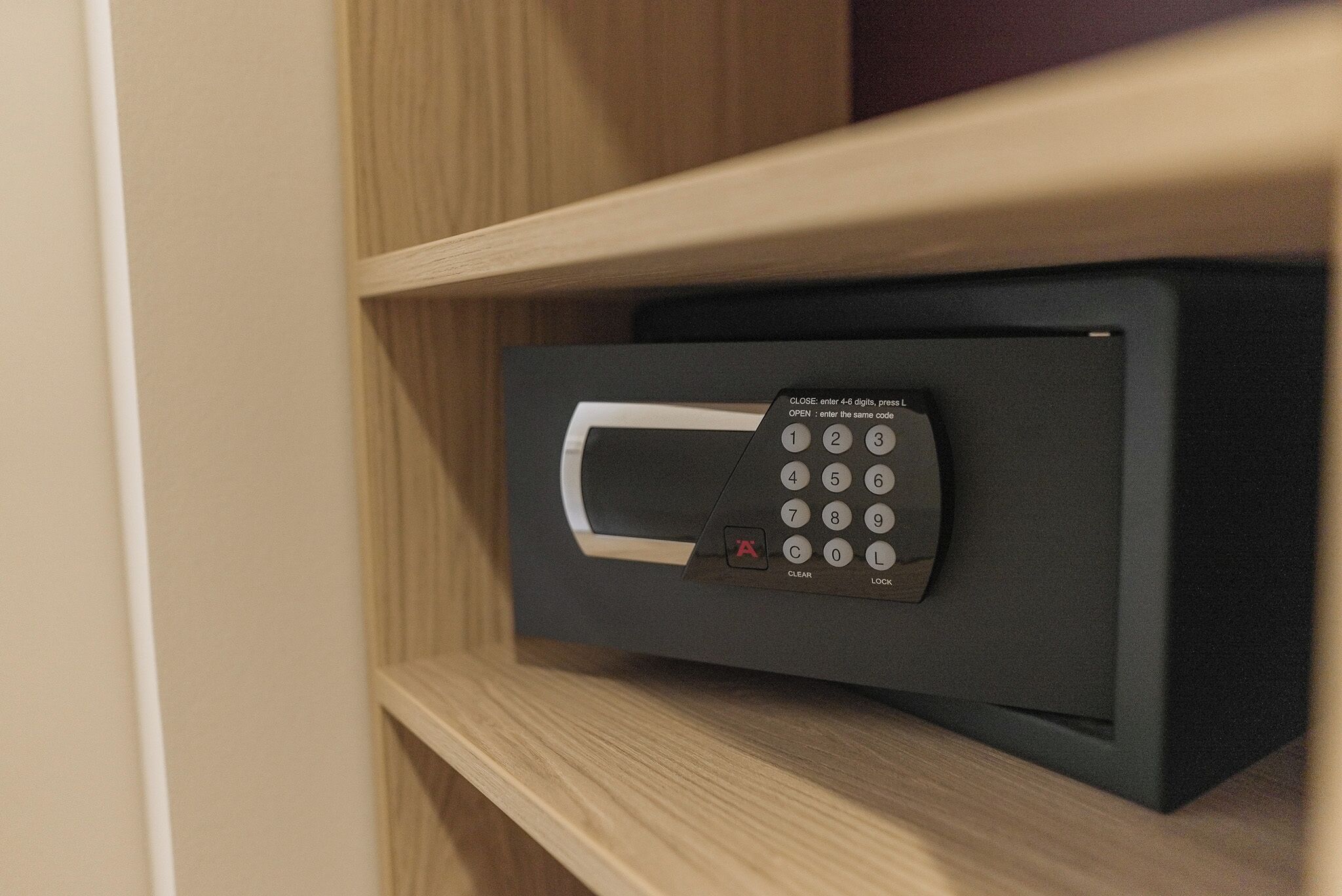 A black electronic device with a keypad and a small screen, mounted on a wooden shelf.