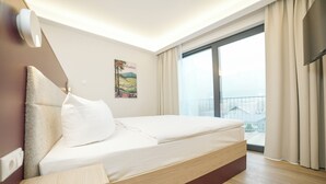Une chambre moderne avec un grand lit, une table de chevet, une lampe fixée au mur, une fenêtre avec des rideaux et une vue sur le paysage urbain.