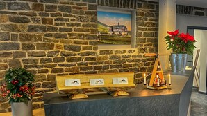 Un comptoir d’accueil avec un mur en pierre en arrière-plan, un tableau encadré et un petit autel orné de bougies.