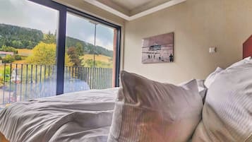 Ein Schlafzimmer mit großem Fenster, einem Bett mit weißer Bettwäsche und einem Gemälde an der Wand.