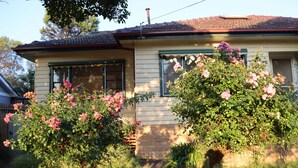 A house with a brick foundation, a tiled roof, and a front yard with flowering bushes. - Humble Abode near Train Station, Costco, Eastland (Heathmont)