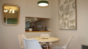A dining area with a round table, white chairs, a mirror, a pendant light, and a wall with a geometric pattern. - Humble Abode near Train Station, Costco, Eastland (Heathmont)