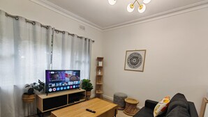 A modern living room with a flat-screen TV, wooden coffee table, black sofa, and a small side table with a plant. - Humble Abode near Train Station, Costco, Eastland (Heathmont)