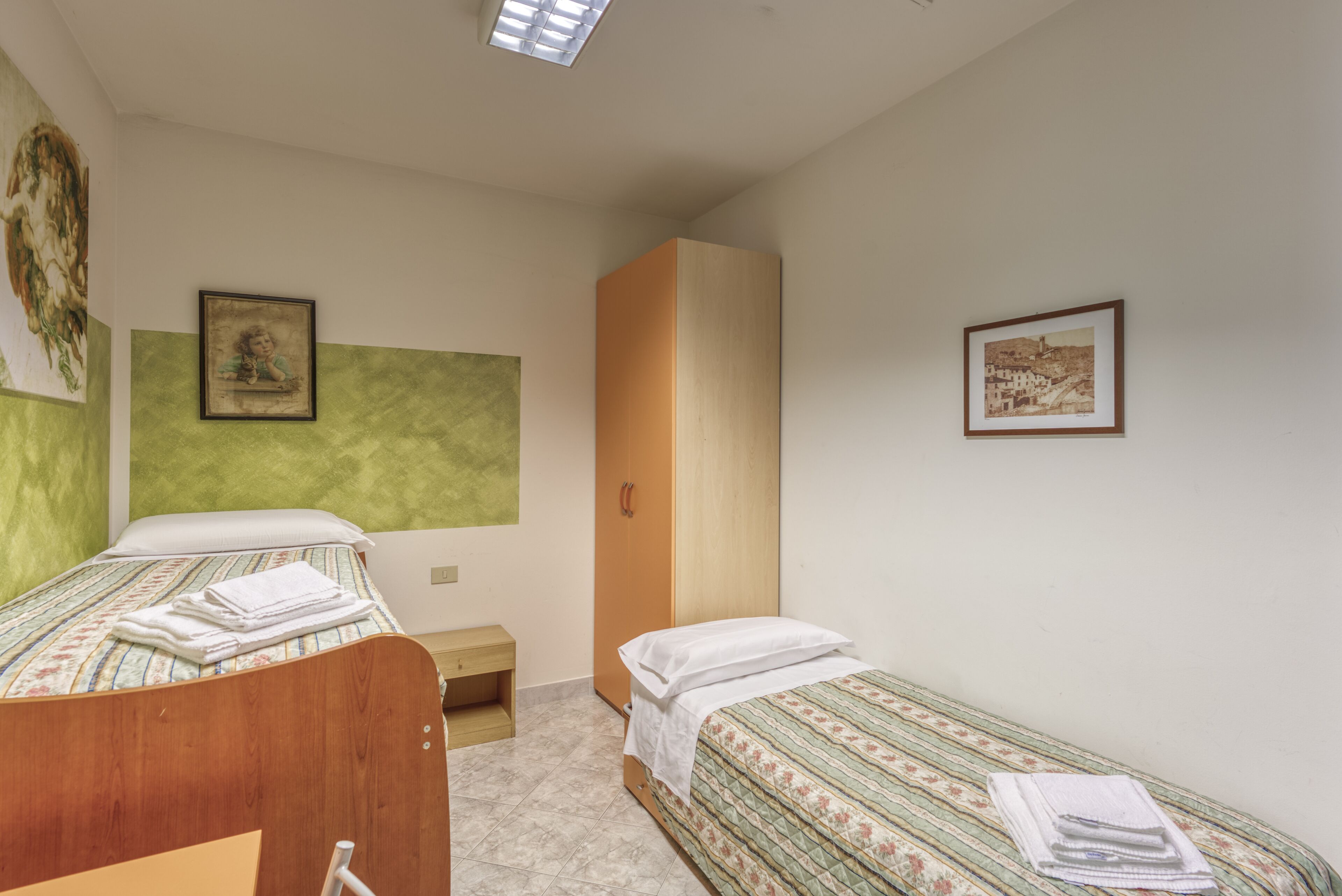 A bedroom with two single beds, a wooden wardrobe, a small bedside table, and a green accent wall.