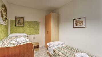 A bedroom with two single beds, a wooden wardrobe, a small bedside table, and a green accent wall.