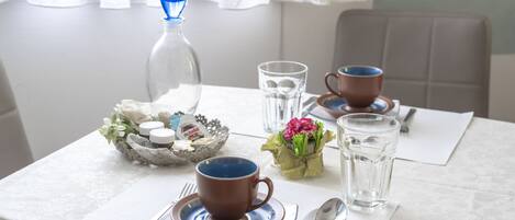Una mesa con una taza marrón, un vaso transparente, una botella y un pequeño jarrón con flores.
