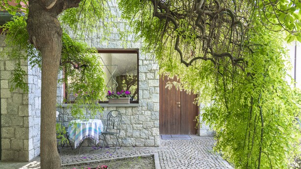 Un bâtiment en pierre avec une porte en bois, un banc et une table recouverte d’une nappe.
