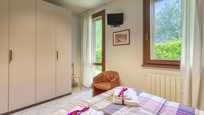 Une chambre à coucher comprenant un lit, une chaise, une armoire, un téléviseur et une fenêtre donnant sur un paysage verdoyant.