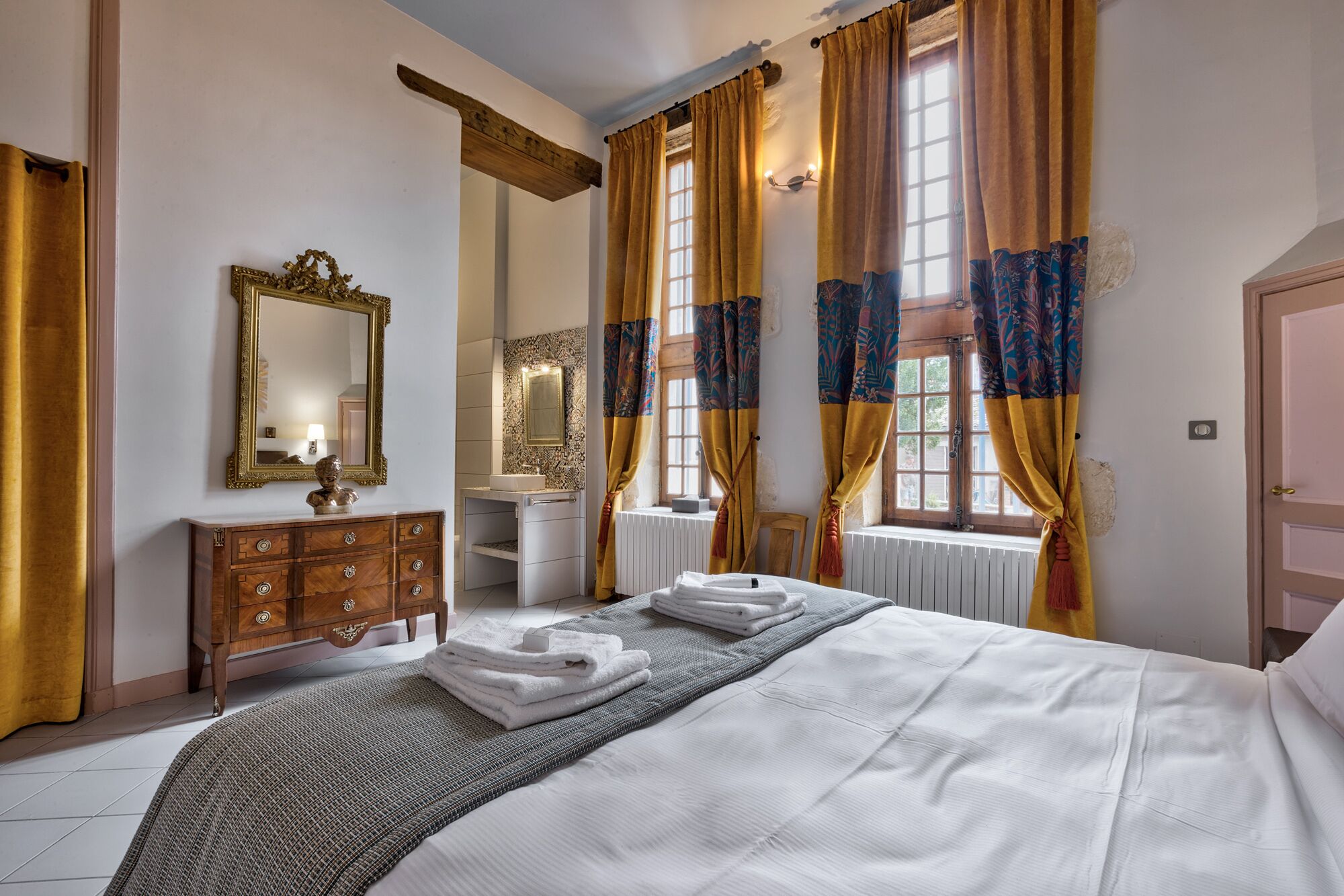 Een hotelkamer met een bed, een houten dressoir, een spiegel en een raam met gordijnen.