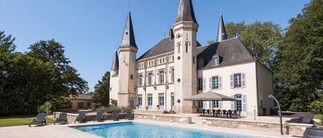 A large building with two towers, a swimming pool, and outdoor seating.