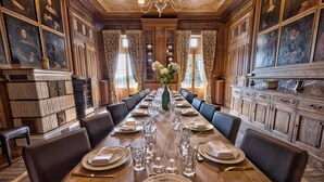 Une salle à manger élégante, avec une longue table dressée pour un repas, bordée de boiseries et agrémentée d’œuvres d’art.
