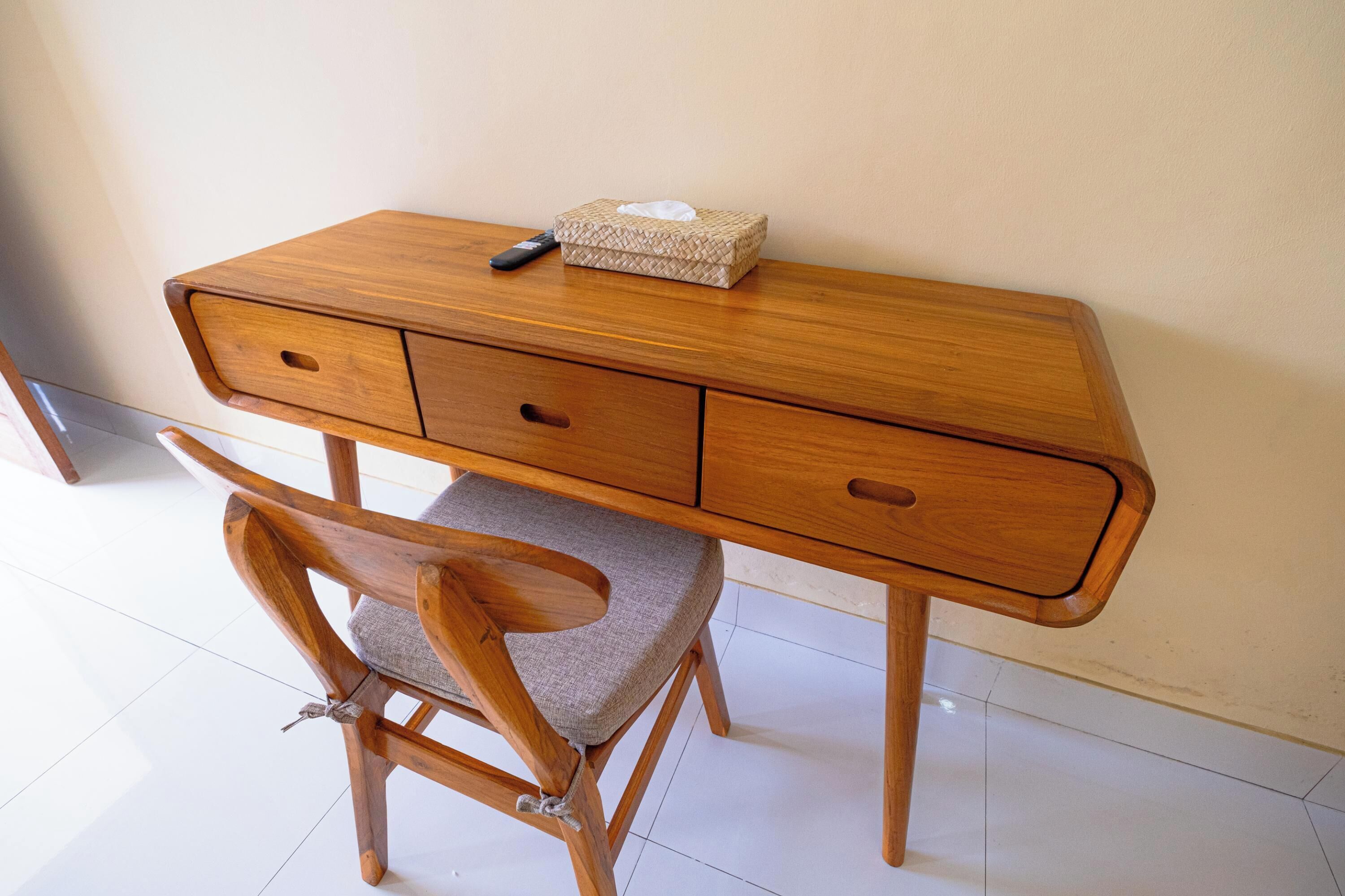 Un escritorio de madera con una caja de pañuelos trenzada y un control remoto encima.