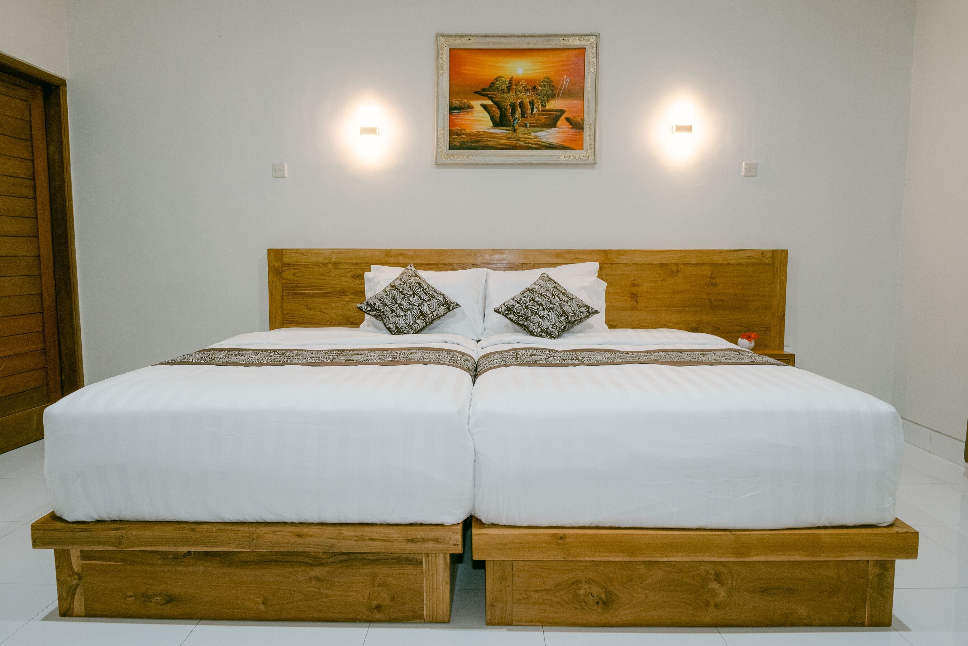 Een tweepersoonsbed met een houten hoofdbord, wit beddengoed en twee decoratieve kussens.
