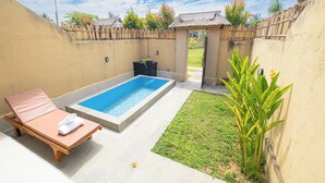 Un área pequeña de piscina al aire libre con una tumbona, un jardín pequeño y una estructura de techo de paja.