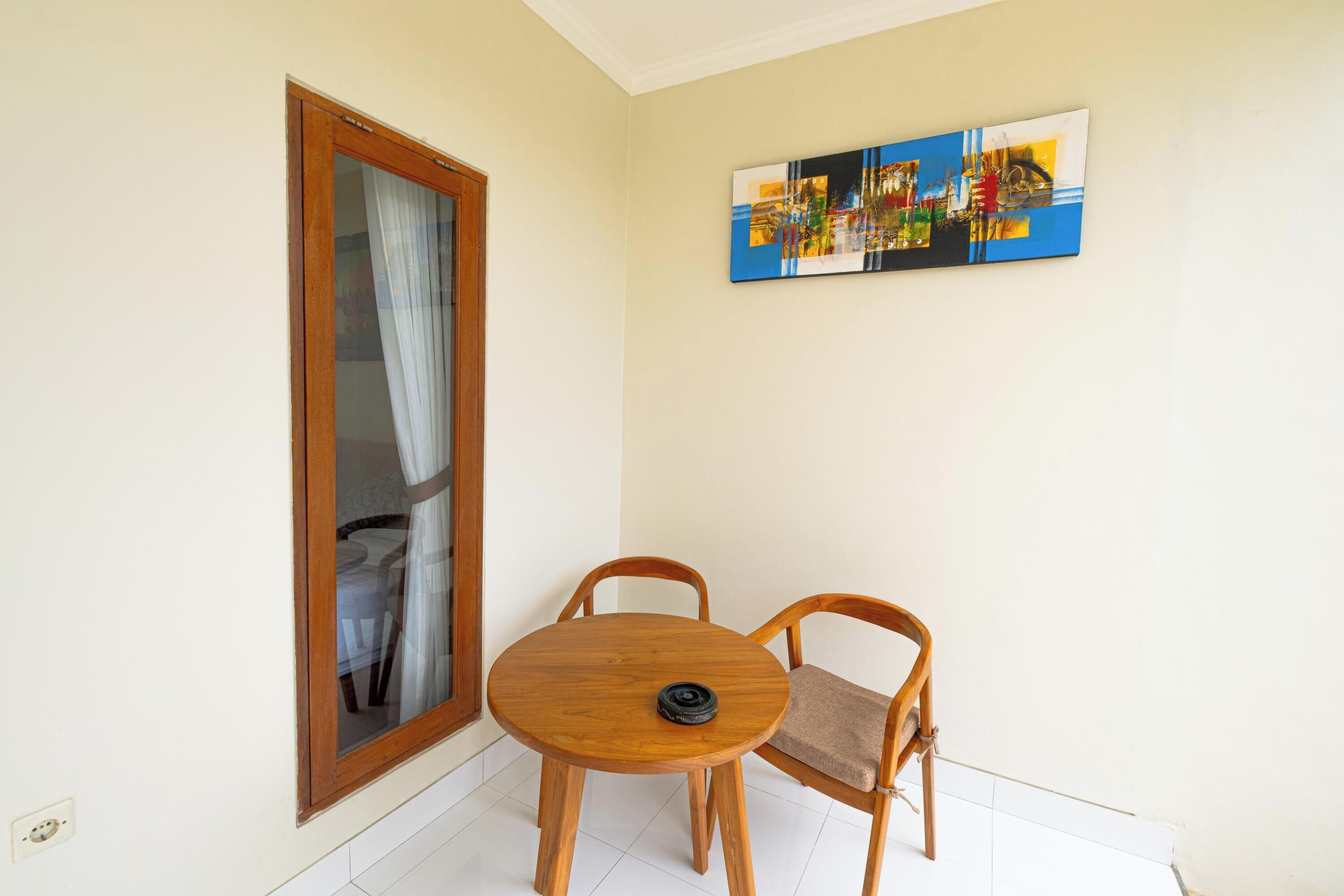 A small room with a wooden table and two chairs, a sliding glass door, and a colorful abstract painting on the wall.