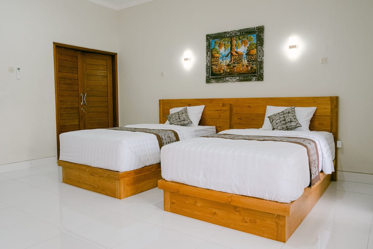 Una habitación con dos camas de madera, ropa de cama blanca, una puerta de madera y un cuadro enmarcado en la pared.