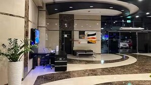 A modern lobby with a curved reception desk, a seating area, and a glass entrance to the parking area.