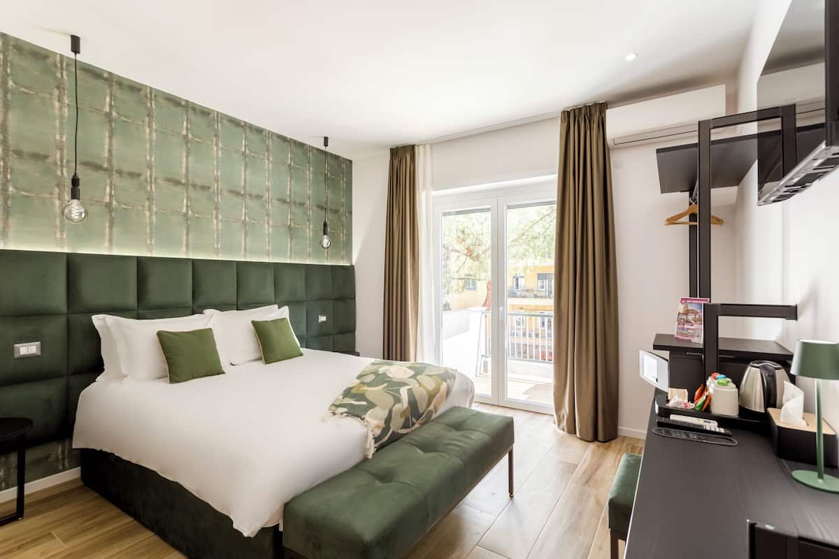 A modern hotel room with a large bed, a desk, and a balcony with curtains.