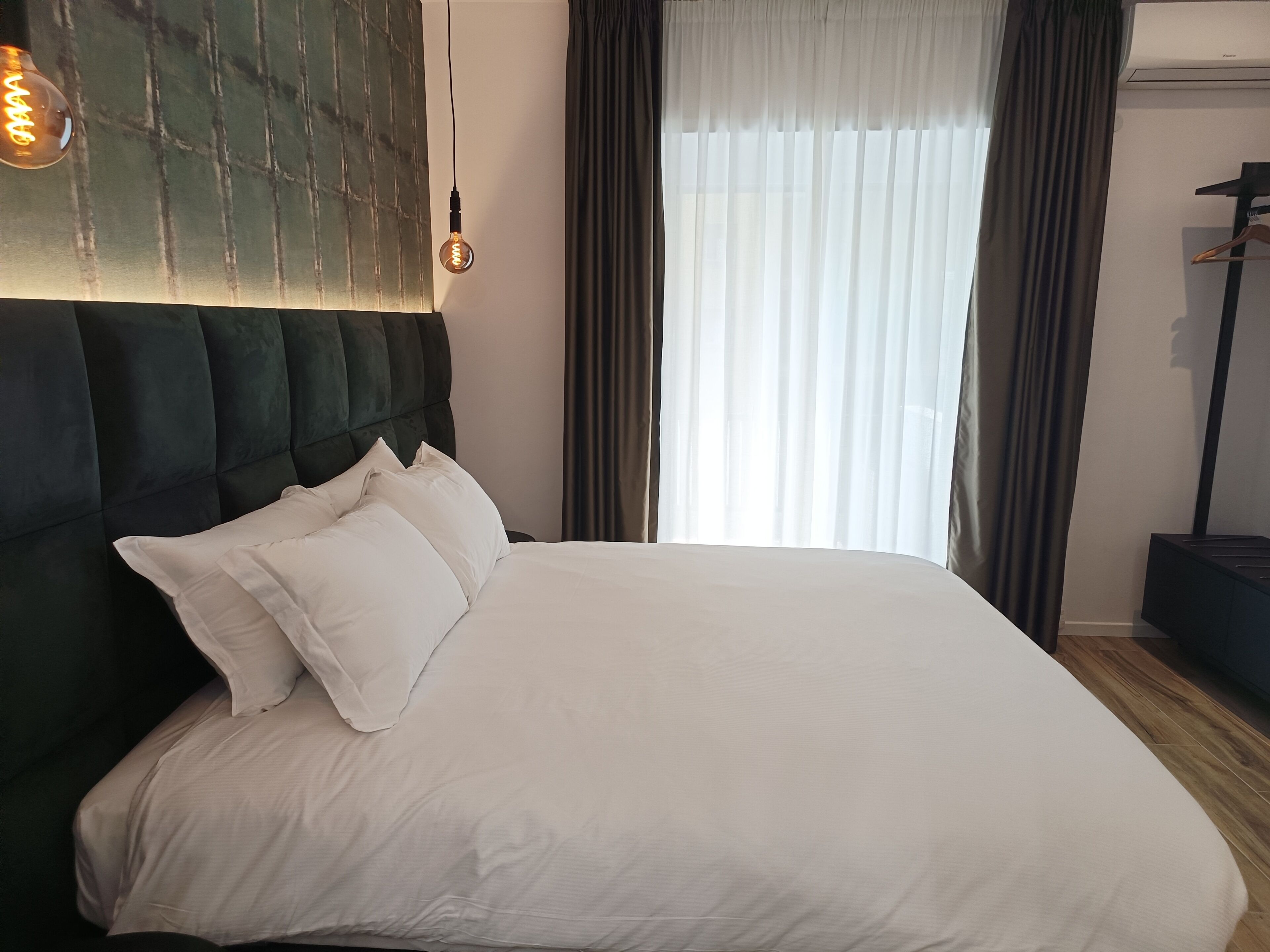 A neatly made bed with white linens and a dark upholstered headboard.