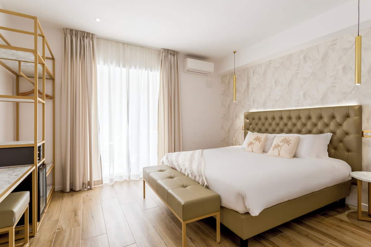 A modern bedroom with a large bed, a bench, a desk, and a wardrobe.