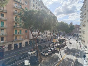 A multi-story building with balconies, a street with parked cars, and a pedestrian walkway. - Romi Suite (Rome)