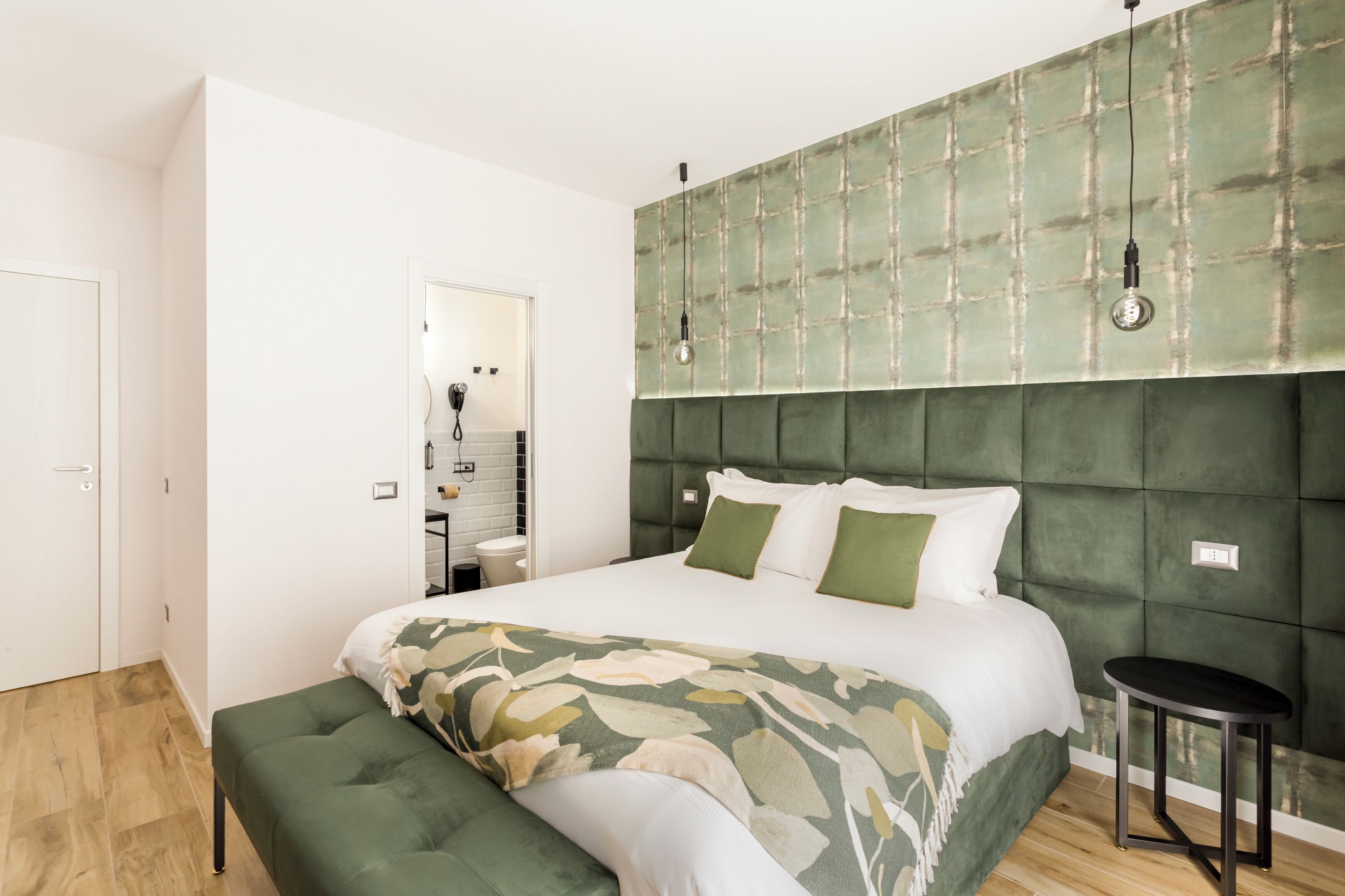 Un dormitorio moderno con una cama grande, un cabecero tapizado en verde, una mesita de noche y un espejo.