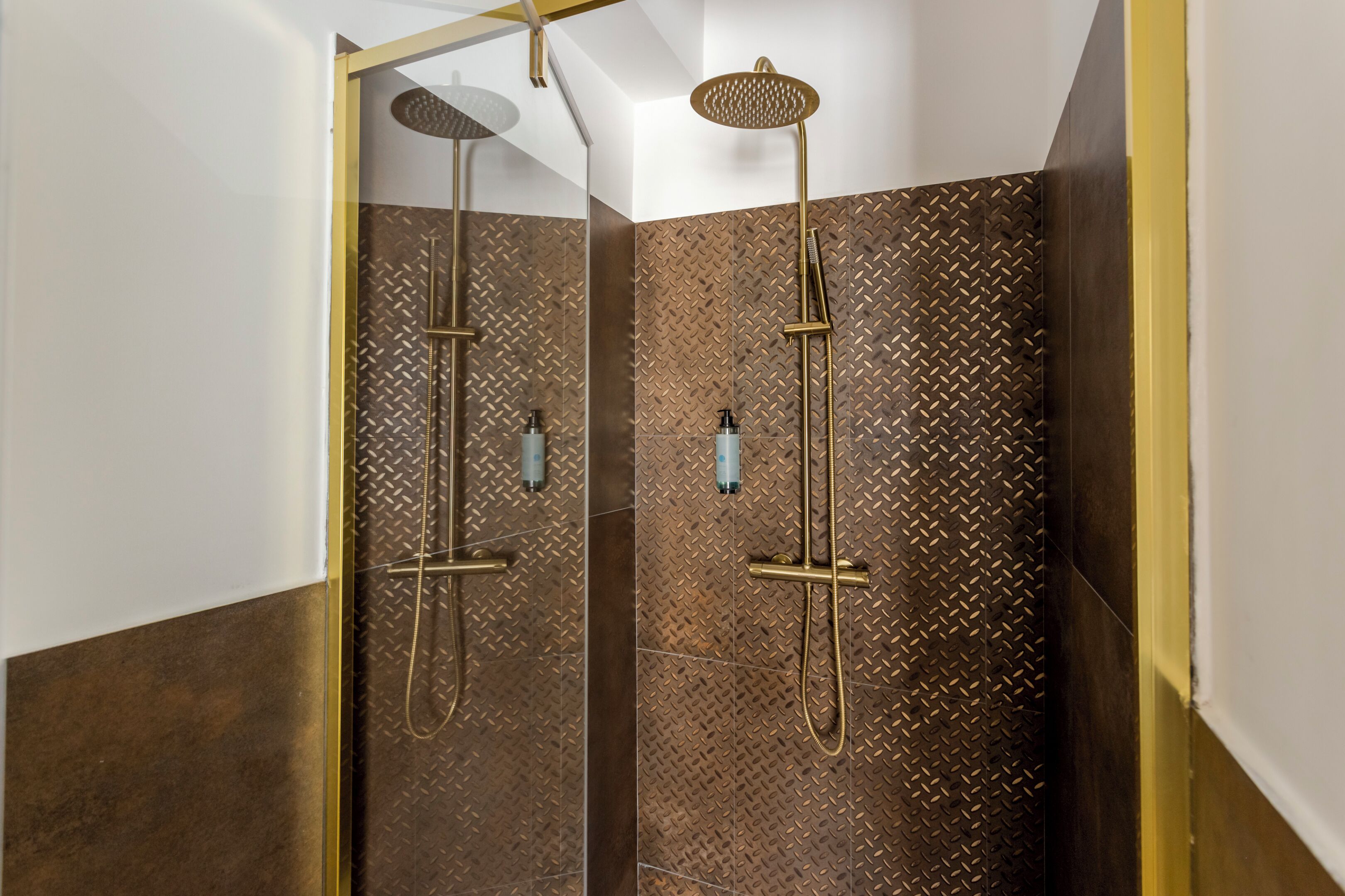 Een moderne douche met een gouden douchekop en handdouche, voor een getextureerde wand.