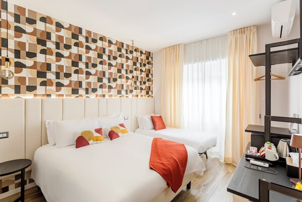 A hotel room with two beds, a desk with a computer and a coffee maker, a wall-mounted air conditioner, and a patterned wall. - Romi Suite (Rome)