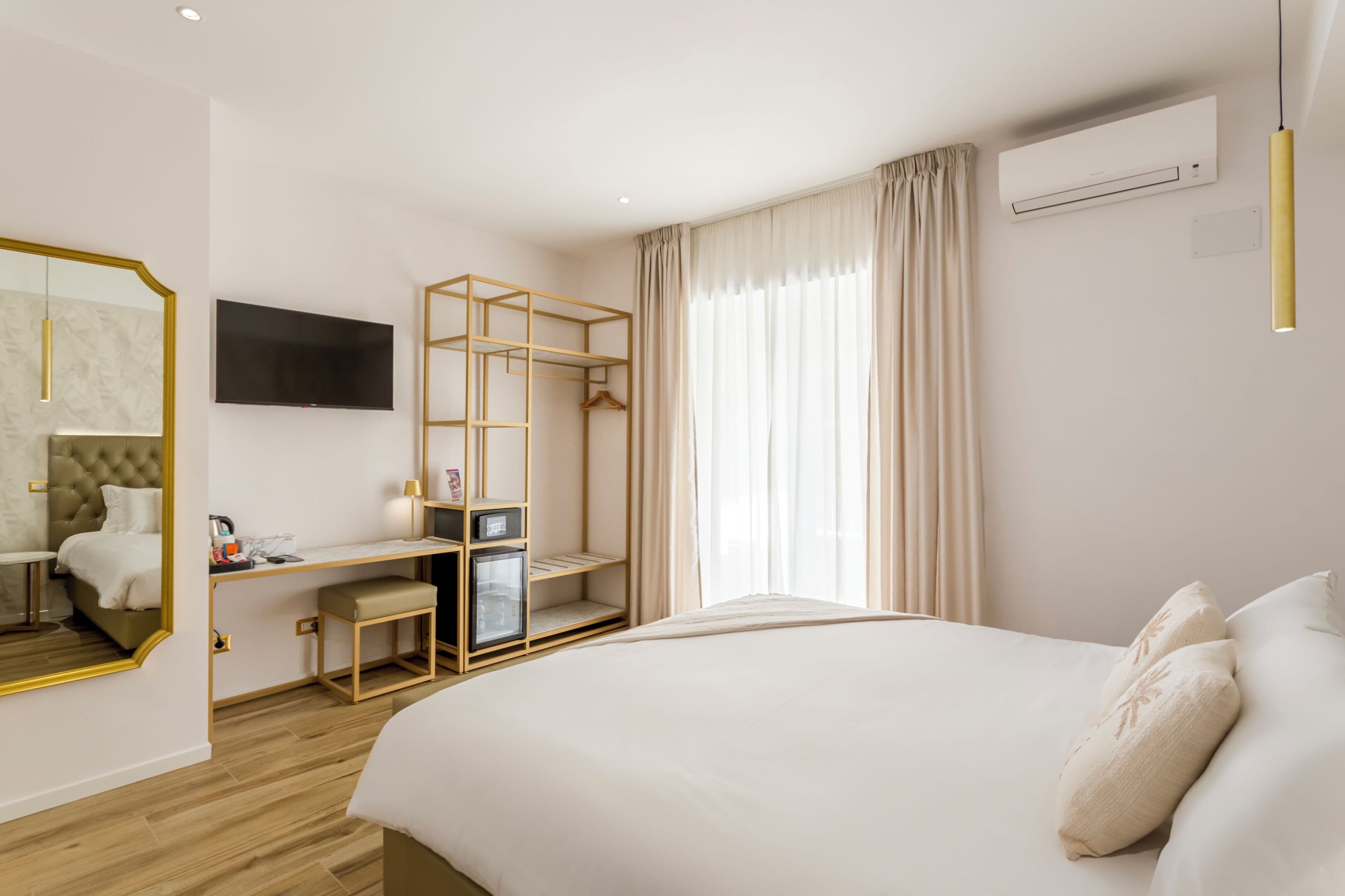 A modern hotel room with a large bed, a desk with a chair, a TV, and a wardrobe.