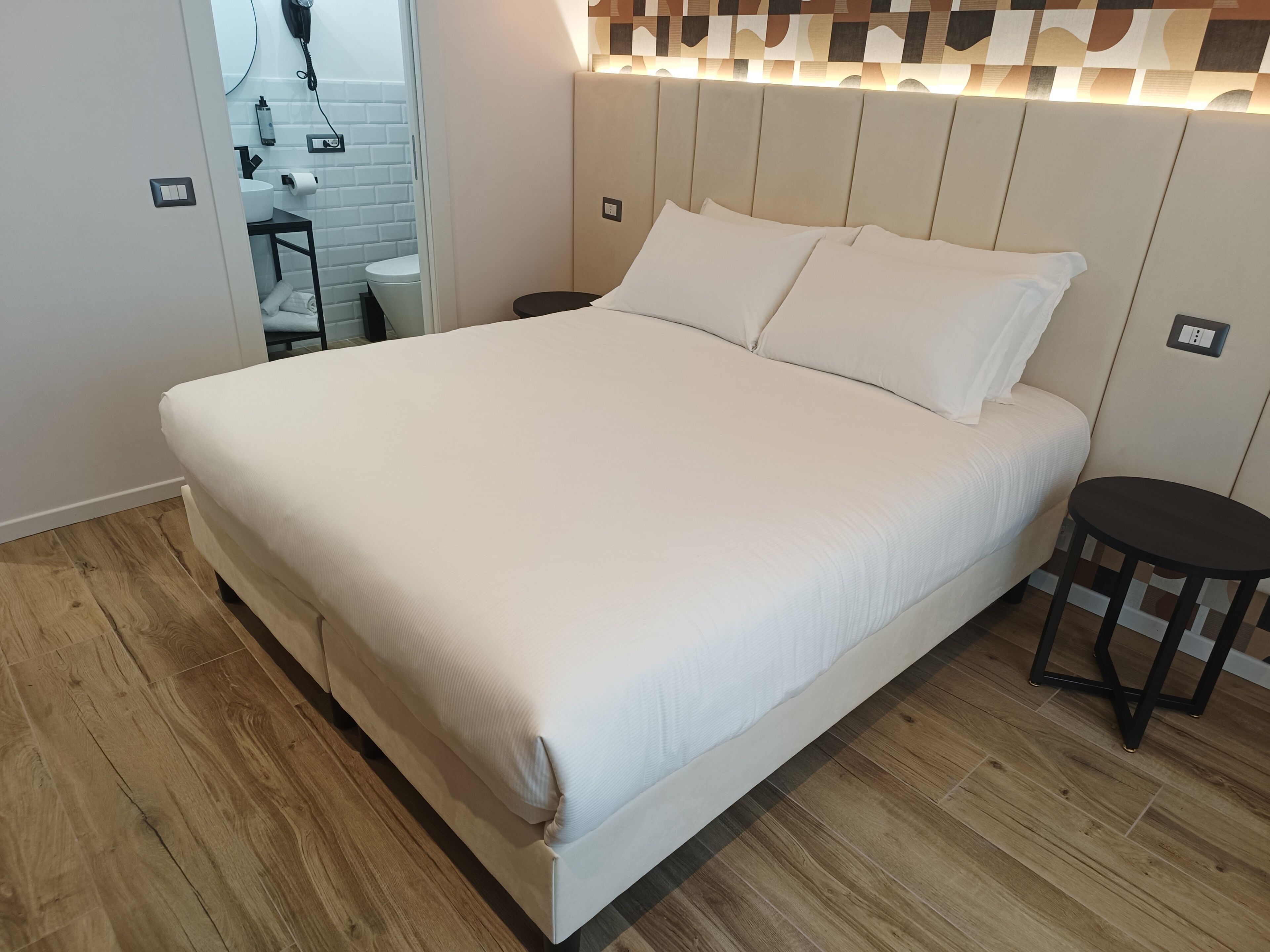 A neatly made bed with a headboard, a small round table, and a wooden floor.